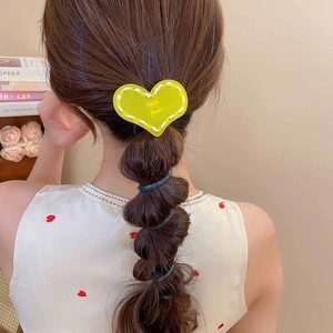 Détail d'un accessoire cheveux cœur jaune en acrylique avec imprimé M sur tresse bulle