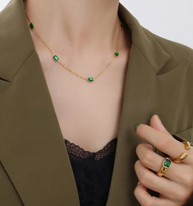 Detail view of 18K gold necklace and emerald ring set worn by model in chic olive blazer