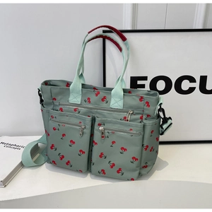 Detail of green tote bag with cherry prints featuring multiple front zipper pockets