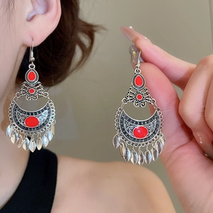 Close-up of ethnic silver bell fringe earrings with red gems and leaf charms on model