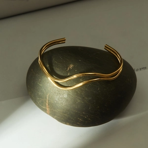 Minimalist double-layered wavy gold open cuff bracelet displayed on a green natural stone