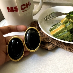 Close-up of retro oval stud earrings with black resin center and gold-toned matte frame