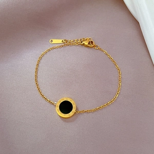 Macro detail of gold-plated stainless steel bracelet with roman numeral black shell pendant
