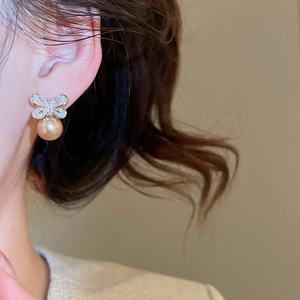 Close-up of elegant zircon bow earrings with champagne pearls on a female model