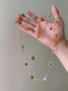 Close-up of golden multi-color faceted beaded necklace held by hand on grey background