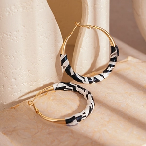 Detail of gold hoop earrings featuring elegant black and white pleated leather wrapping