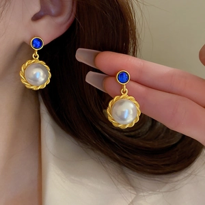 Close-up of gold earrings with white pearls and blue stones worn by a model