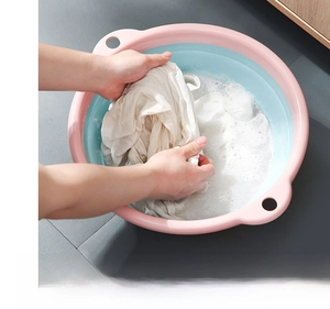 Action shot of washing white clothes with soap foam in a foldable pink and blue basin