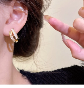 Close-up of elegant gold stud earring with white stone and crystals on female model