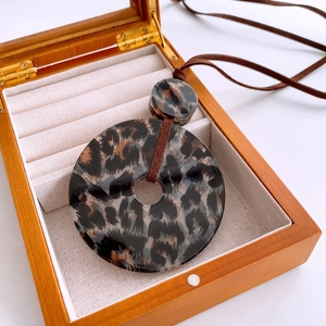 Detail of leopard print acrylic round pendant with brown cord in a wooden gift box