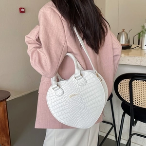 Weiße Herz-Handtasche mit Krokodilmuster und Gold-Logo getragen zu einem schicken Rosa Blazer