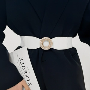 Close-up of a white elastic waist belt with a sparkling gold rhinestone round buckle