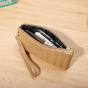 Minimalist straw woven clutch bag with wrist strap and zipper closure on wooden background
