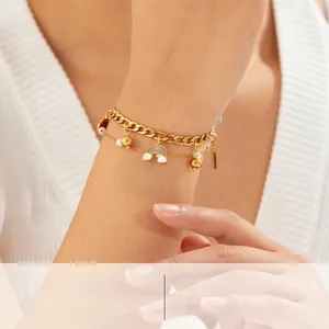 Detail of a double-layered gold chain bracelet with rainbow, gold bead and pearl charms