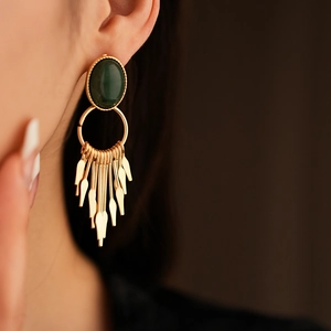 Detail of vintage gold earrings with dark green gemstone and dangling metallic tassels