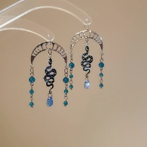 Detail of bohemian snake earrings featuring crystal fringe tassels and blue moon accents