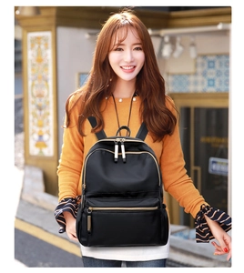 Street style shot of a woman wearing a black nylon backpack with metallic zippers