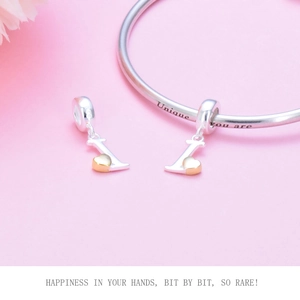 Macro detail of silver bangle featuring gold heart charm and 'Unique you are' engraving
