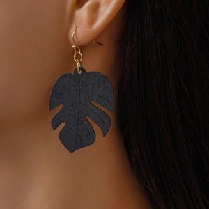 Close-up of black monstera leaf wooden earring worn by model with golden hook detail