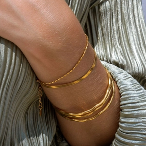 Detailed view of stacked 18K gold wave bangles and sleek snake chain on a model wrist