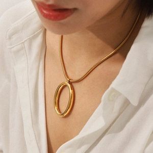 Close-up of gold snake chain necklace with oval pendant on a model wearing white shirt