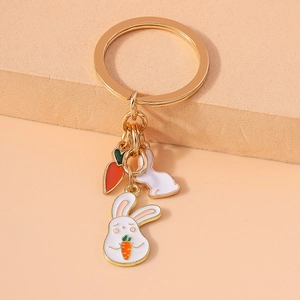 Detailed macro view of a gold-tone metal keychain featuring white enamel rabbits and carrots