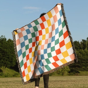 Outdoor model holding large colorful checkered woven blanket with decorative fringes