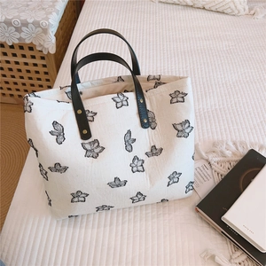 Détail du sac cabas en toile crème avec broderie papillon et poignées en cuir