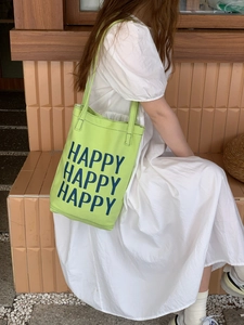 Side view of a green canvas tote bag with Happy Happy Happy print worn by a model