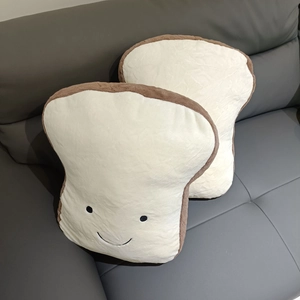 Close-up of two soft toast bread plush pillows with smiling faces on a grey leather sofa