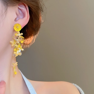 Detailed close-up of yellow beaded flower tassel earrings worn by a model in soft light