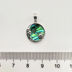 Close-up of a silver moon and star pendant with shell inlay next to a measuring ruler