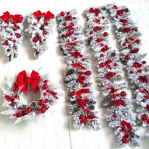 Flat lay of snowy Christmas wreath, garlands, and teardrop swags with red ornaments