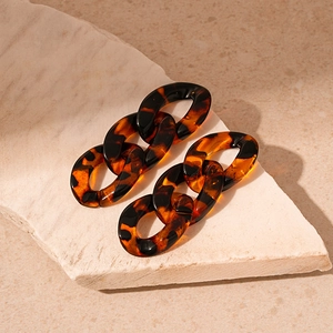 Detailed close-up of tortoise shell acrylic chain drop earrings on a stone base