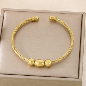 Detailed view of golden twisted steel wire bangle with polished beads in a jewelry box