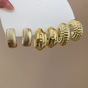 Macro shot of three pairs of textured gold C-shaped earrings on a white display card