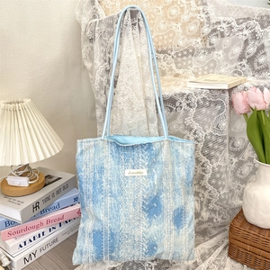 Detail of blue tie-dye lace tote bag with brand label and long shoulder straps