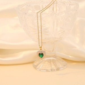 Collier cœur doré avec pierre verte et cristaux sur un verre décoratif