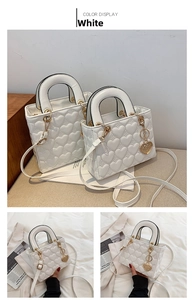 Detailed view of white heart-quilted handbag featuring elegant gold-tone hardware and charms