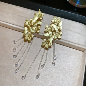 Macro view of gold flower and butterfly earrings with long silver tassel and crystals