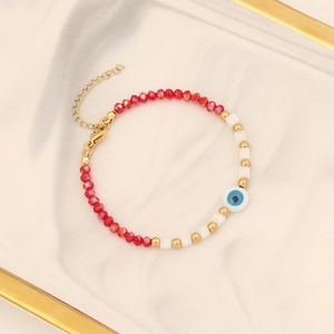 Handmade beaded eye bracelet with red and white beads on a gold-rimmed ceramic plate