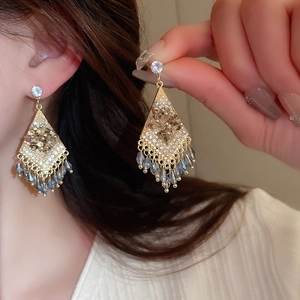 Primer plano de pendientes boho en forma de rombo con borde dorado y flecos elegantes