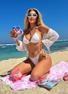 Close-up of white three-piece bikini set with sheer lace cover-up on sunny beach sand