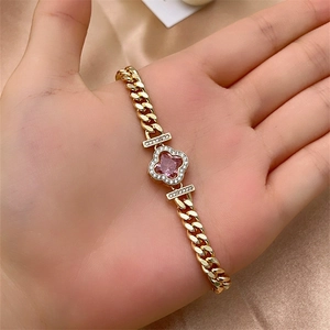 Gold Cuban link bracelet with a sparkling pink zircon clover pendant on champagne silk