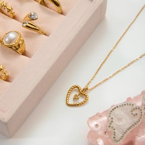 Golden woven heart necklace and assorted rings presented in a luxury velvet jewelry box
