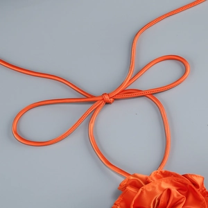 Detail of orange satin halter neck dress with intricate bow knot and 3D floral accent