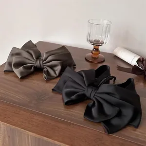 Detail of satin bow banana clips in coffee brown and black on a wooden table