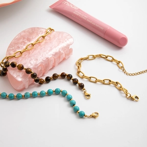Detail of tiger eye and turquoise bead bracelets with gold chain on marble background