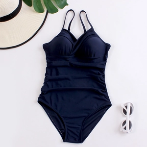 Flat lay of navy blue ruched one-piece swimsuit with summer accessories on white background