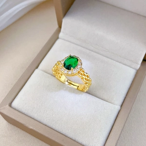 Close-up of emerald ring with gold watch-chain band and diamond halo in jewelry box